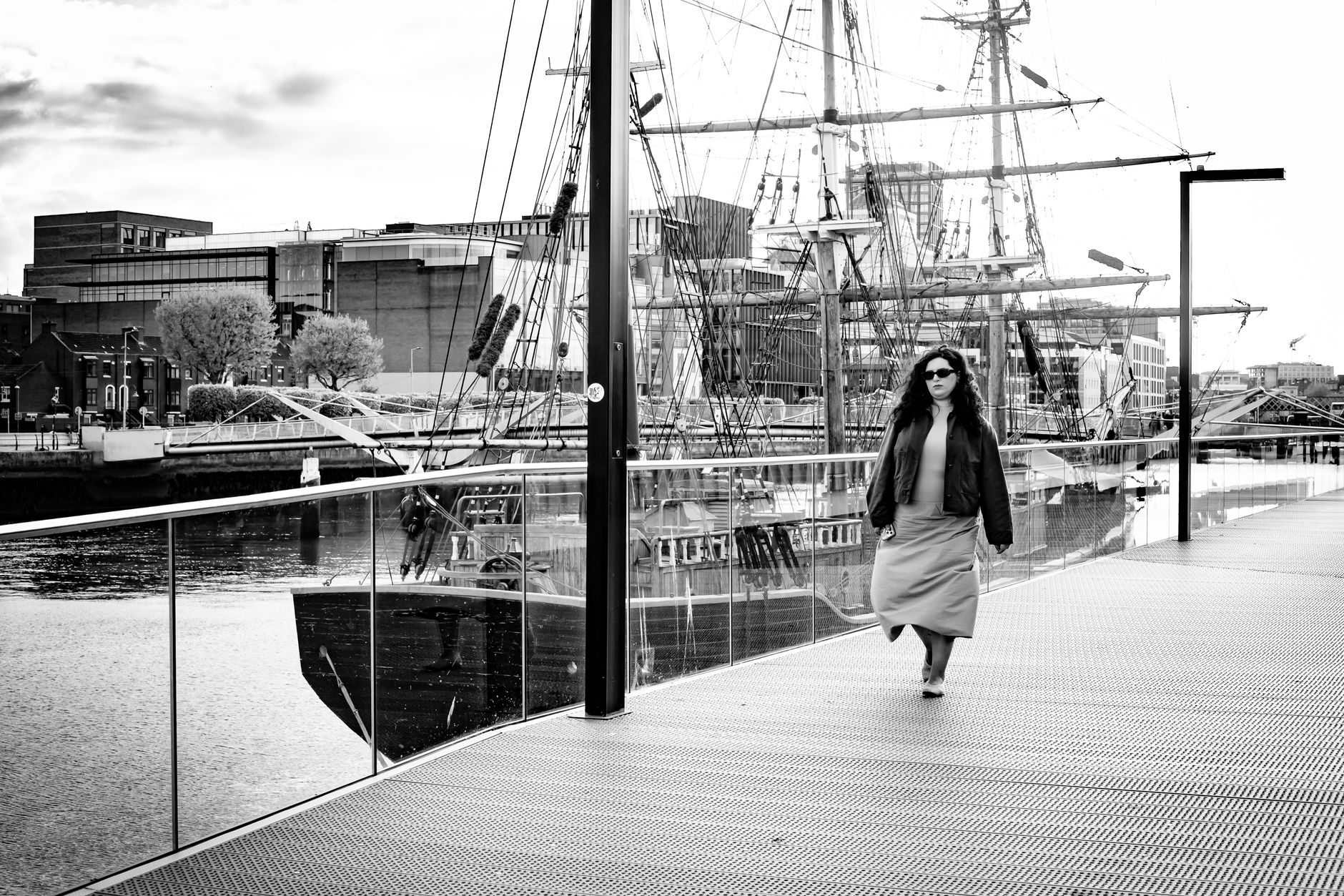 Une femme marche d'un pas soutenu le long d'un quai bordé de voiliers